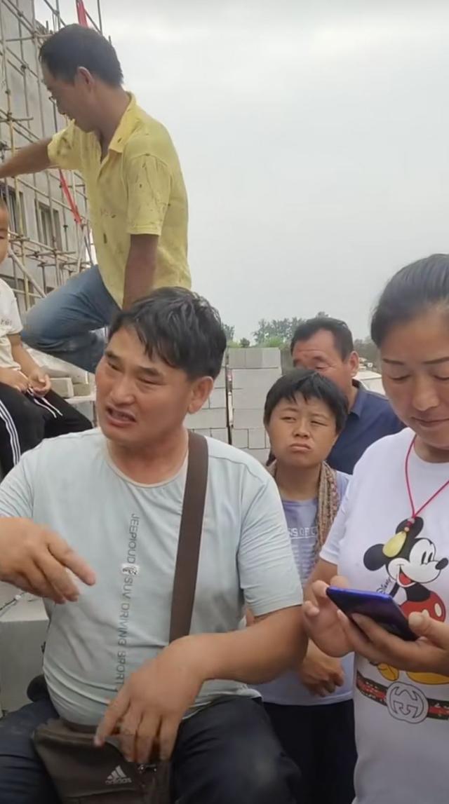 大衣哥耐心教村民唱歌，身后未建成小楼抢镜，唱歌干活两不误