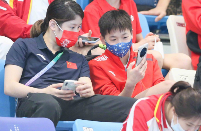 全红婵现身看台！目睹国家队师哥夺冠，戴卡通口罩，专注玩手机